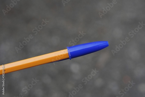 one long plastic orange pen closed with a blue cap on a gray background