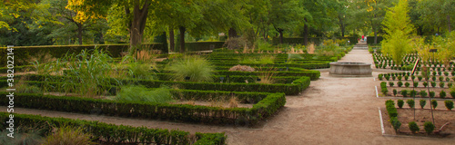 Vista panorámica de un jardín botánico. Camino con una fuente ornamental redonda, parterres separados que albergan diferentes tipos de plantas, flores y árboles.