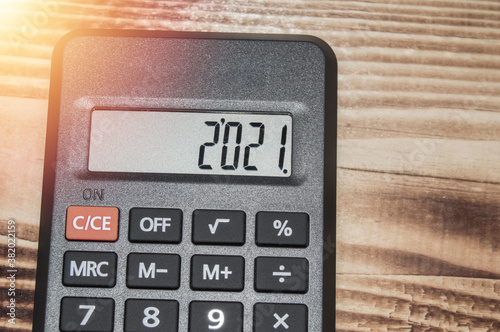 Black electronic calculator on dark wooden background, numbers show 2021