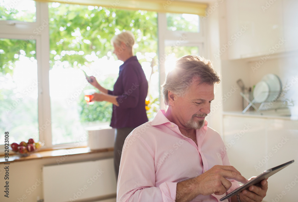 Senior man using digital tablet in sunny morning kitchen Senior man using digital tablet in sunny morning kitchen