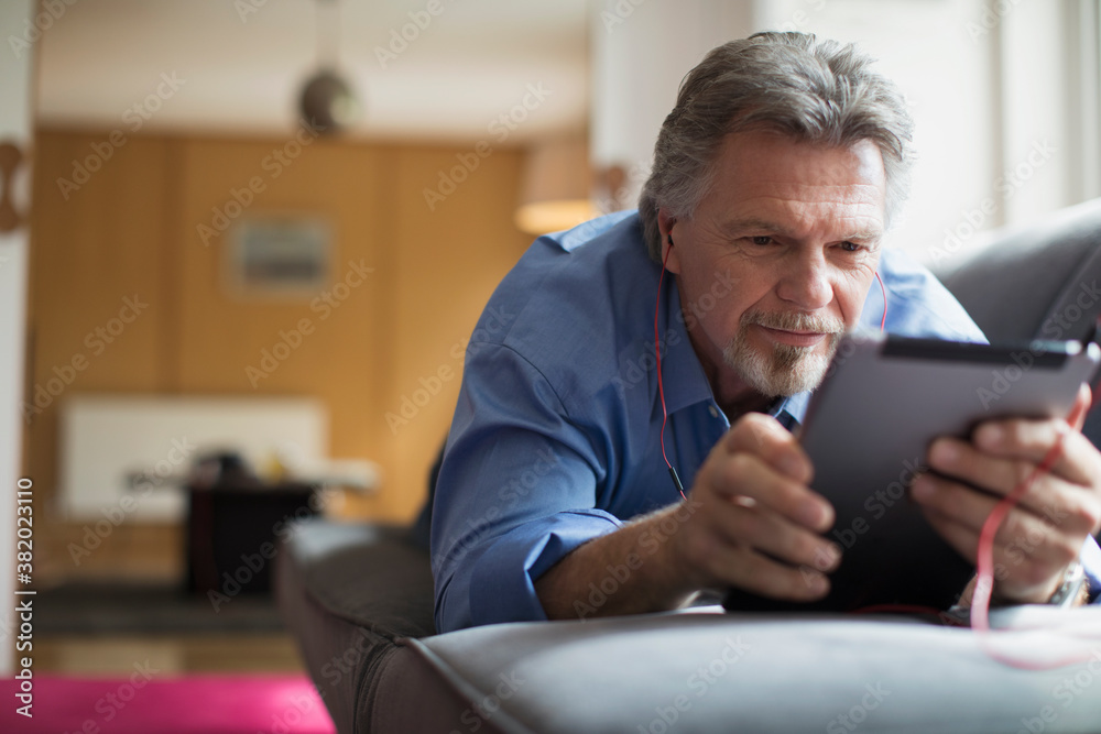 Senior man using headphones and digital tablet on living room sofa