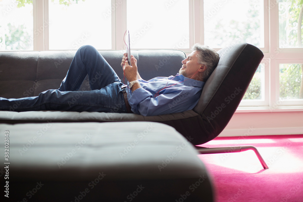 Senior man relaxing with digital tablet on living room sofa Senior man relaxing with digital tablet on living room sofa