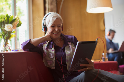 Happy senior woman using headphones and digital tablet on sofa photo