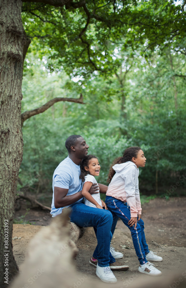 Happy father and daughters sitting on fallen log in woods Happy father and daughters sitting on fallen log in woods
