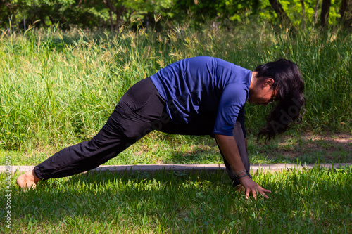 Young Hispanic woman practicing yoga outdoors in a park with trees, very concentrated and relaxed © Antonio Tanaka