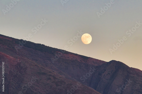 Full moon rising behind a ridge of the west maui mountains.