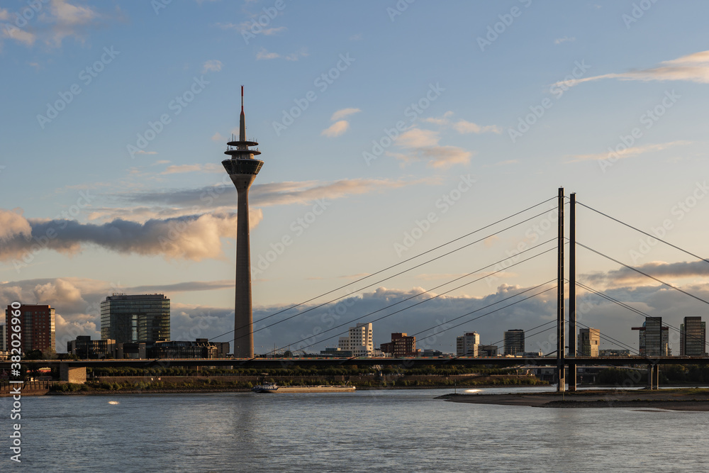 Outdoor scenery of city skyline, downtown district, Rhein tower, suspension bridge and Rhine River against beautiful golden sunset sky in Düsseldorf, Germany. 