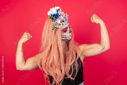 young beautiful woman wearing halloween make up over red background showing arms muscles smiling proud. Fitness concept.