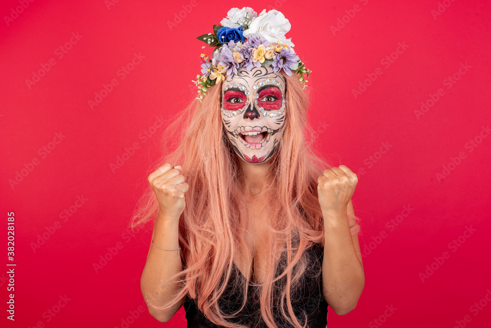Young beautiful woman wearing halloween make up over red background celebrating surprised and amazed for success with arms raised and open eyes. Winner concept. Young beautiful woman wearing halloween make up over red background celebrating surprised and amazed for success with arms raised and open eyes. Winner concept.