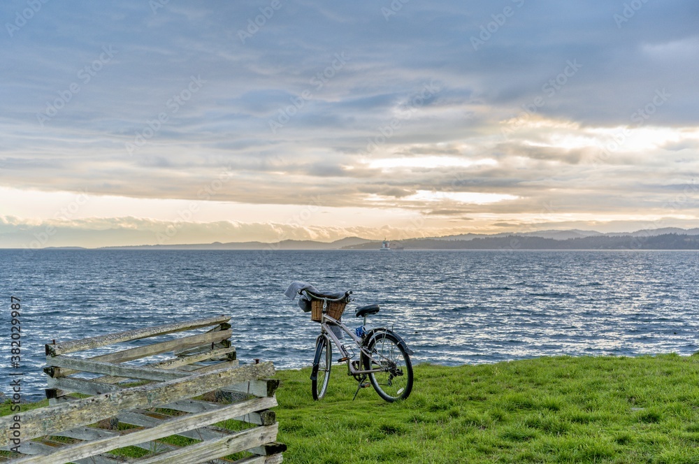 Fototapeta premium Bike parked by wooden fence on a bank above a vast expanse of blue ocean - Esquimalt, Greater Victoria, Vancouver Island, British Columbia, Canada