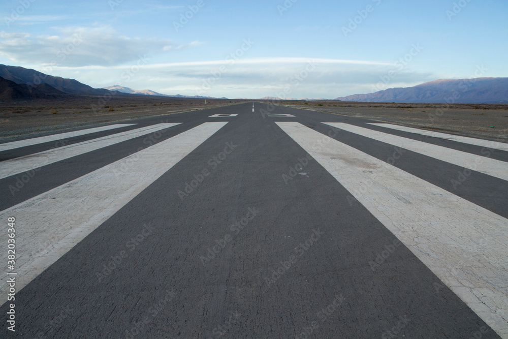 Transport. Wide straight asphalt airdrome road across the desert and into the mountains.