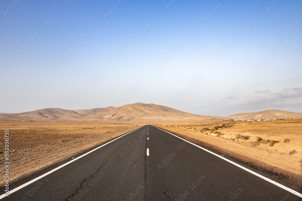 deserted road with mountains in the background in arid landscape on Fuerteventura canary islands.