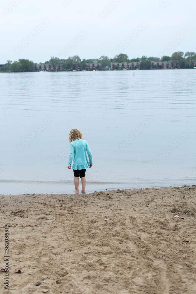 Little girl with blonde curly hair standing at waters edge or lake 