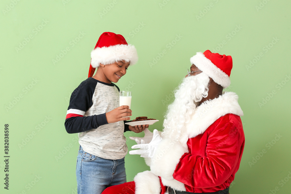 Obraz premium African-American Santa Claus and cute little boy with treat on color background