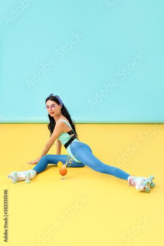 Beautiful young woman on roller skates and with cocktail against color background