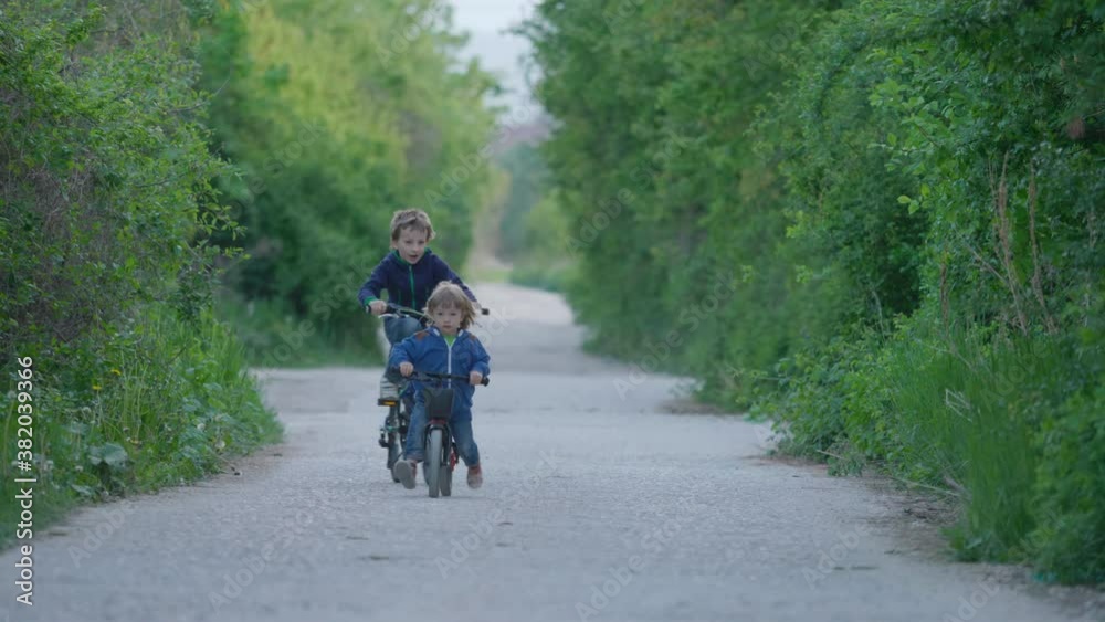 Brother riding bicycles on empty village road, children unequal competition Brother riding bicycles on empty village road, children unequal competition