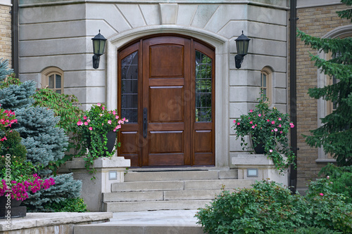 Elegant wooden front door of house with flowers and shrubs