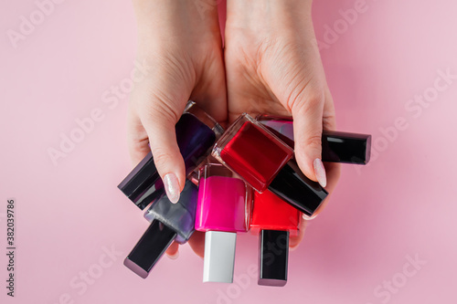 Female hands with bright nail polishes. A group of colored nail enamel on pink background. photo