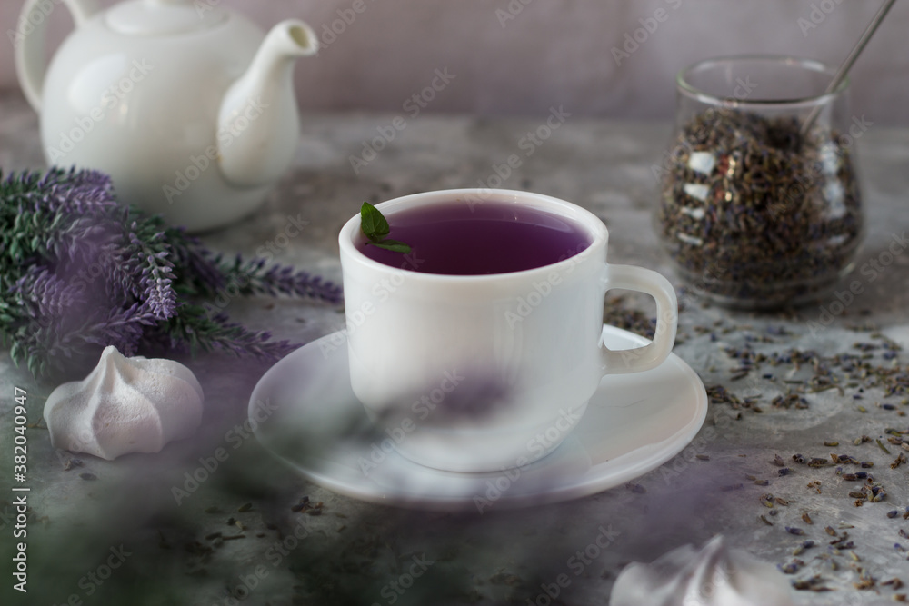 lavender tea in a white mug. Purple tea in a mug on a light background stands on the table next to lavender flowers. Dried lavender flowers are brewed in a Cup. lavender tea in a white mug. Purple tea in a mug on a light background stands on the table next to lavender flowers. Dried lavender flowers are brewed in a Cup.