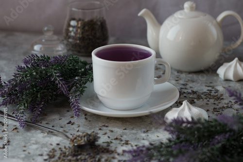 lavender tea in a white mug. Purple tea in a mug on a light background stands on the table next to lavender flowers. Dried lavender flowers are brewed in a Cup.