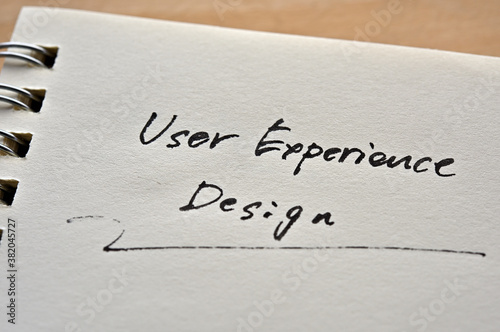 At the edge of the notebook, "User Experience Design" is written. Close-up in direct sunlight.