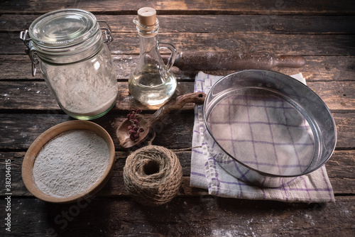 Old rural kitchen table with flour, cooking oil, sieve, towel and rolling pin background.