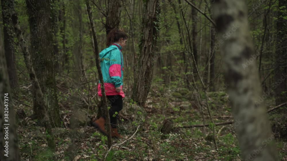 a curious girl walks through the woods in a blue and fuchsia rain jacket
