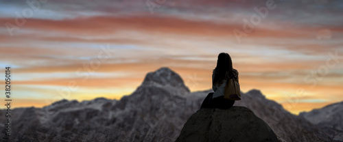 a girl sitting on the mountain peak and beautiful mountains in fog at sunset in summer.