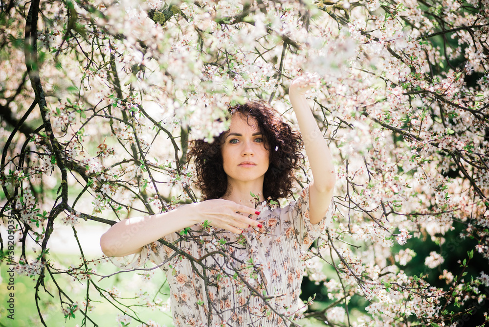 Young attractive woman with curly long hair posing in spring blooming garden, apple trees Young attractive woman with curly long hair posing in spring blooming garden, apple trees