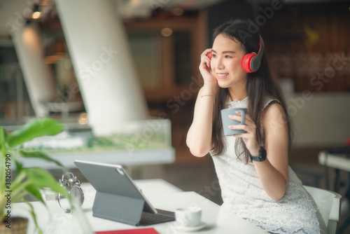 Portrait of female with headphone relaxing with coffee cup while working with mock up tablet in cafe.