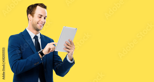 Portrait image - happy smiling businessman using no-name tablet pc, over yellow background. Success in business concept studio picture. Copyspace for some text.