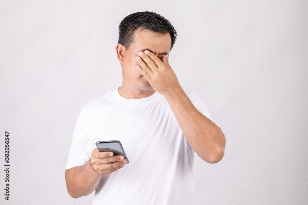 Eyestrain concept. Man touching his eyes because pain or hurt after using too much smartphone. Studio shot isolated on grey Eyestrain concept. Man touching his eyes because pain or hurt after using too much smartphone. Studio shot isolated on grey