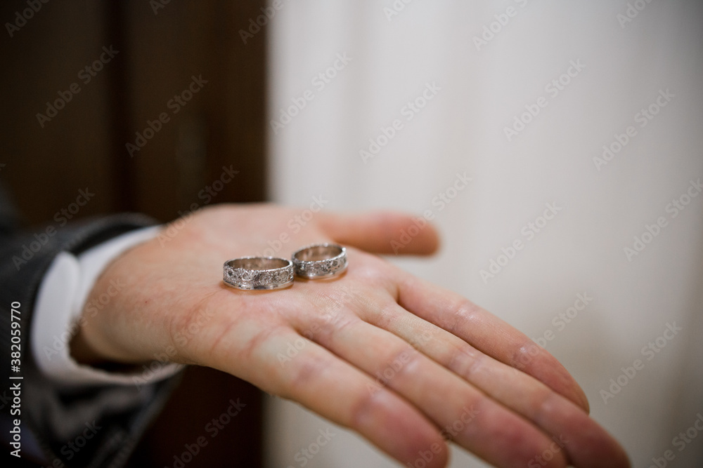 groom in a suit holds wedding rings in his palm