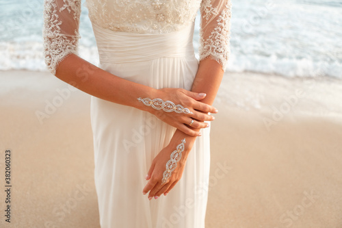 Woman in wedding dress stand on the beach in front ofthe sea, henna art in the bride's hand
