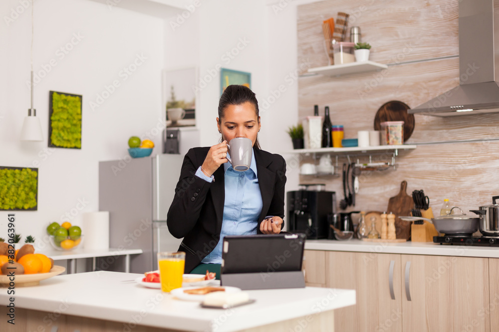 Freelancer enjoing the coffee in the morning in a modern kitchen. Business woman reading the last news online before going to work, using modern technology in the kitchen while eating a healthy meal Freelancer enjoing the coffee in the morning in a modern kitchen. Business woman reading the last news online before going to work, using modern technology in the kitchen while eating a healthy meal
