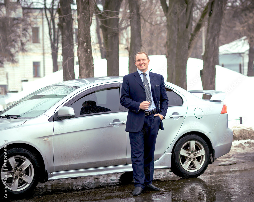 A business man in a strict blue suit by a car on the road in winter. Transport and auto. Business. Copy space on the left