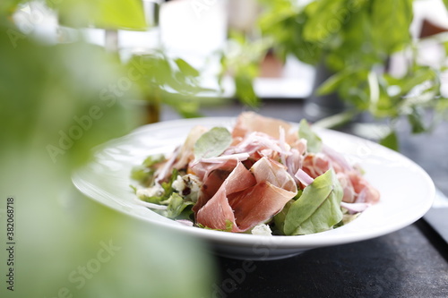 Salad with Parma ham, tomatoes, yellow beetroot, and vinaigrette sauce.
Appetizing dish served on a white plate. culinary photography.

