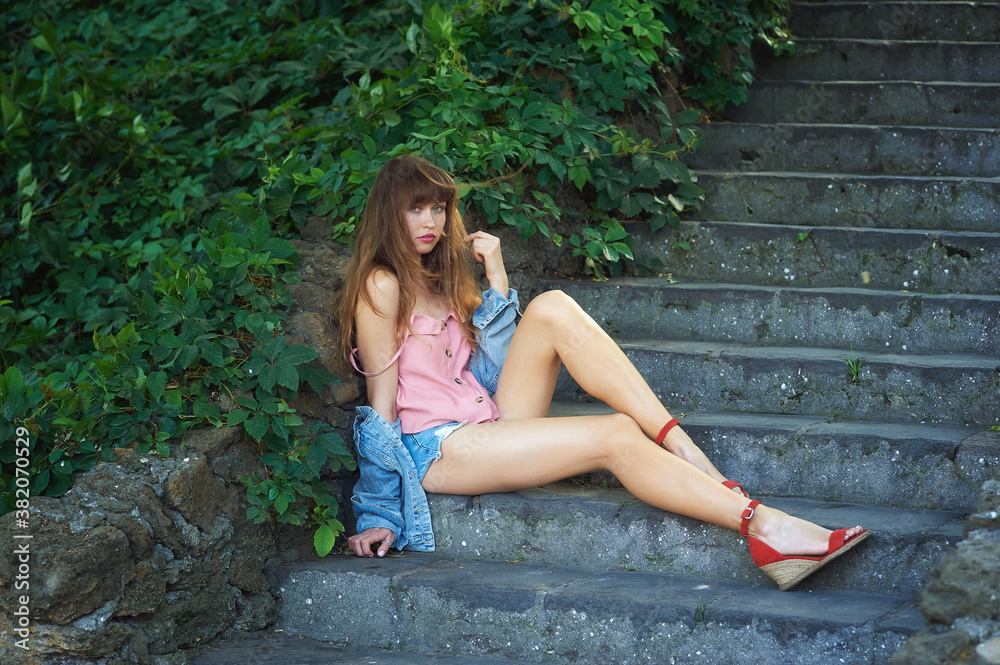 Portrait of a young woman in denim shorts sitting on the steps of an old stone staircase Portrait of a young woman in denim shorts sitting on the steps of an old stone staircase
