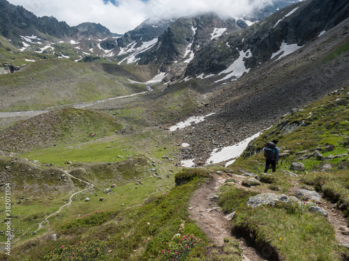 Lonely man hiker at Stubai hiking trail, Stubai Hohenweg at green summer alpine mountain valley in Stubai Tyrol, Austrian Alps photo