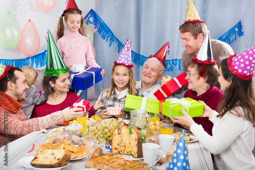 Large family handing gifts to birthday girl during dinner