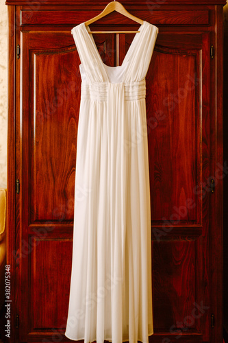 The bride's dress in the Greek style on a hanger on a wooden door.