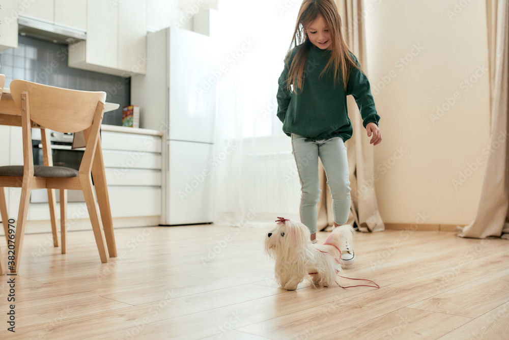 A small girl going after her toy dog in a bright roomy kitchen