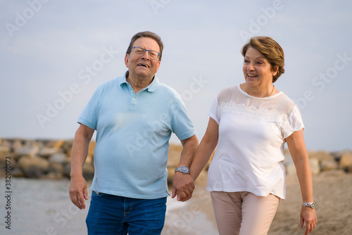 happy retired mature couple walking on the beach - pensioner woman and her husband taking romantic walk together enjoying sweet holidays in lifetime relationship and love