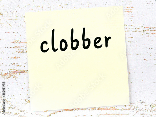 Yellow sticky note on wooden wall with handwritten word clobber