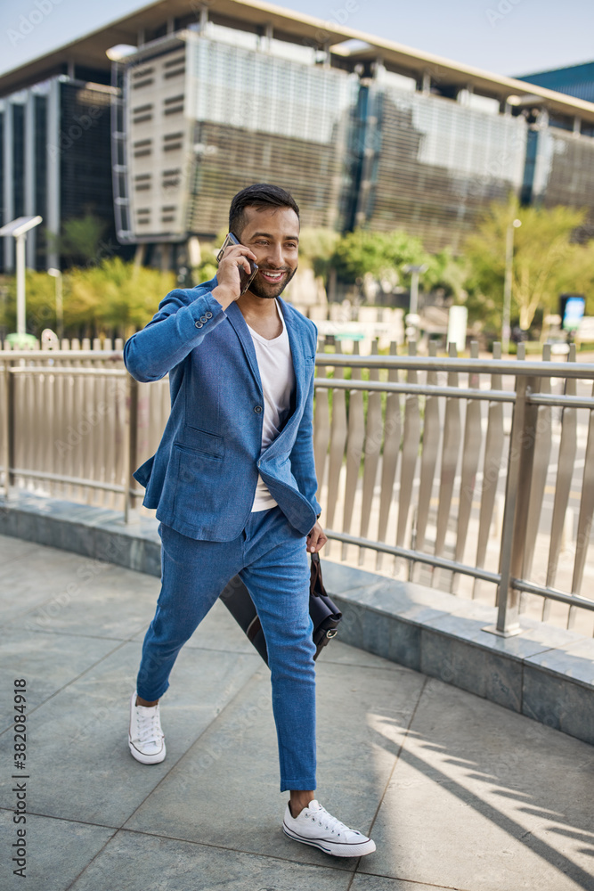 Smiling Indian arabic businessman walking talking on mobile phone in city