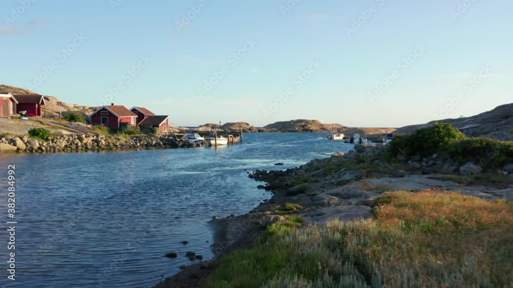 Fishing village on Swedish west coast at blue ocean. Small fisher boats at pier. Sunny evening light over rocks and stones. drone flight close over water surface red cottage shed and fish crab traps Fishing village on Swedish west coast at blue ocean. Small fisher boats at pier. Sunny evening light over rocks and stones. drone flight close over water surface red cottage shed and fish crab traps
