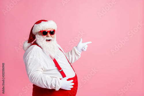 Profile side photo overweight santa claus touch his big abdomen point index finger copyspace x-mas ads wear sunglass sunspenders overall headwear isolated pastel color background