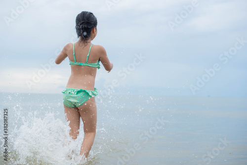 Little  girl playing on the beach on summer holidays. Children in nature with beautiful sea, sand and blue sky. Happy kids on vacations at seaside running in the water. . © nareekarn