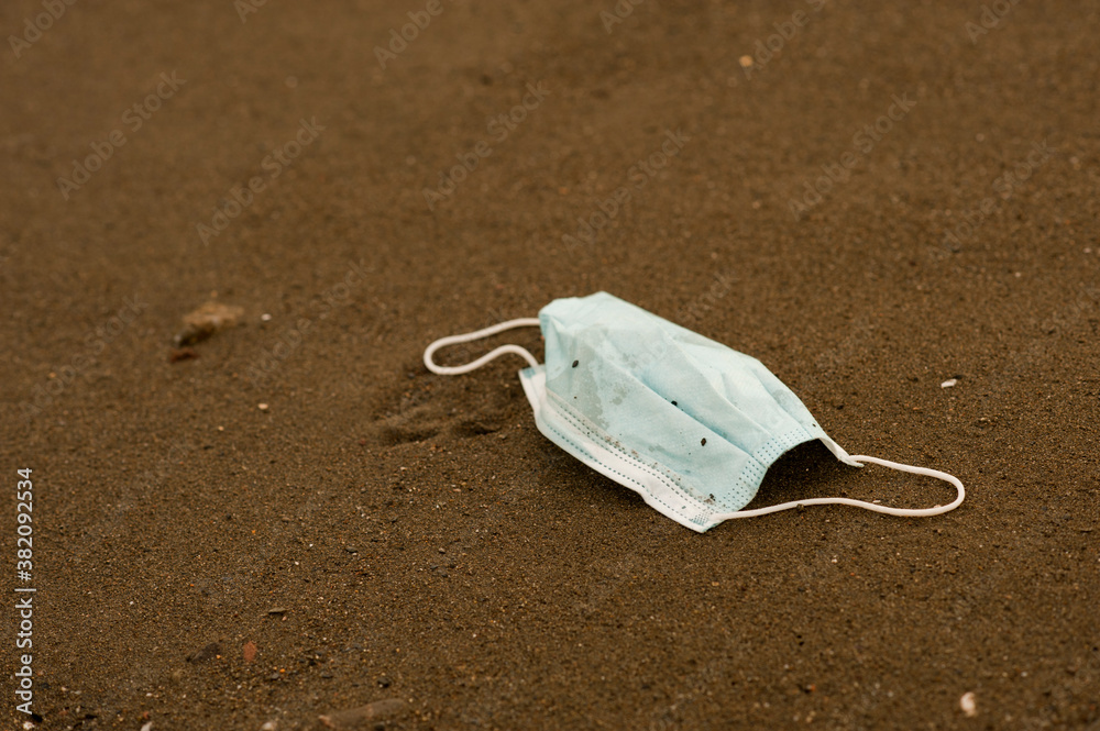 Waste during COVID-19 with sand in the background. Dumped into oceanic coronavirus single-use face masks. Environmental and coastal plastic pollution. Garbage on the beach Waste during COVID-19 with sand in the background. Dumped into oceanic coronavirus single-use face masks. Environmental and coastal plastic pollution. Garbage on the beach