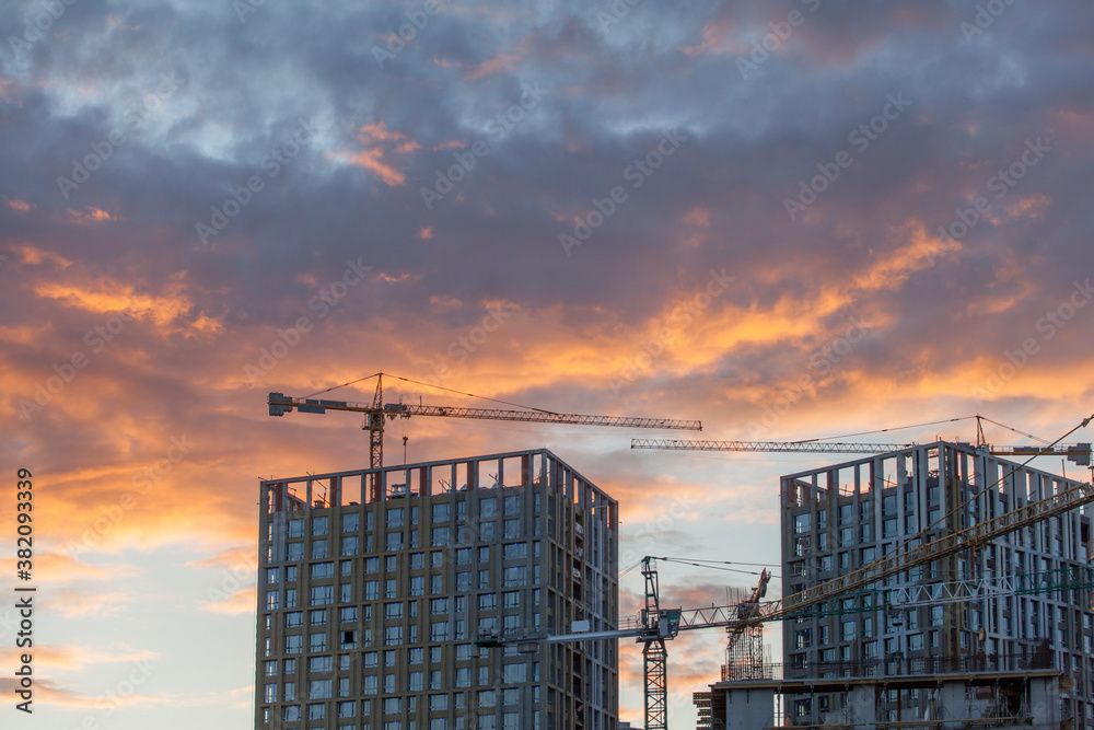 construction cranes against the background of bright evening clouds construction cranes against the background of bright evening clouds